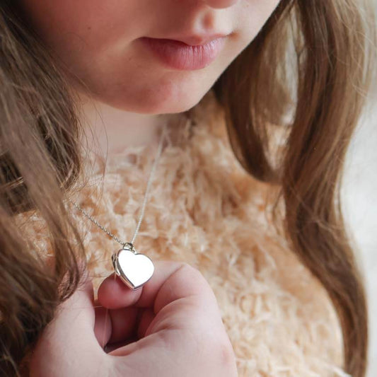 Model wearing silver heart shaped locket on a silver chain.
