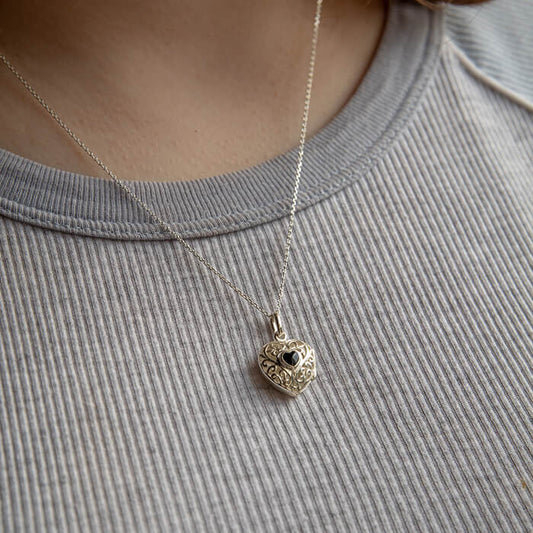 Silver necklace with a heart-shaped pendant on a person wearing a gray shirt.