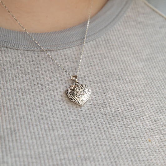 Model in grey wearing a. heart shaped photo locket necklace