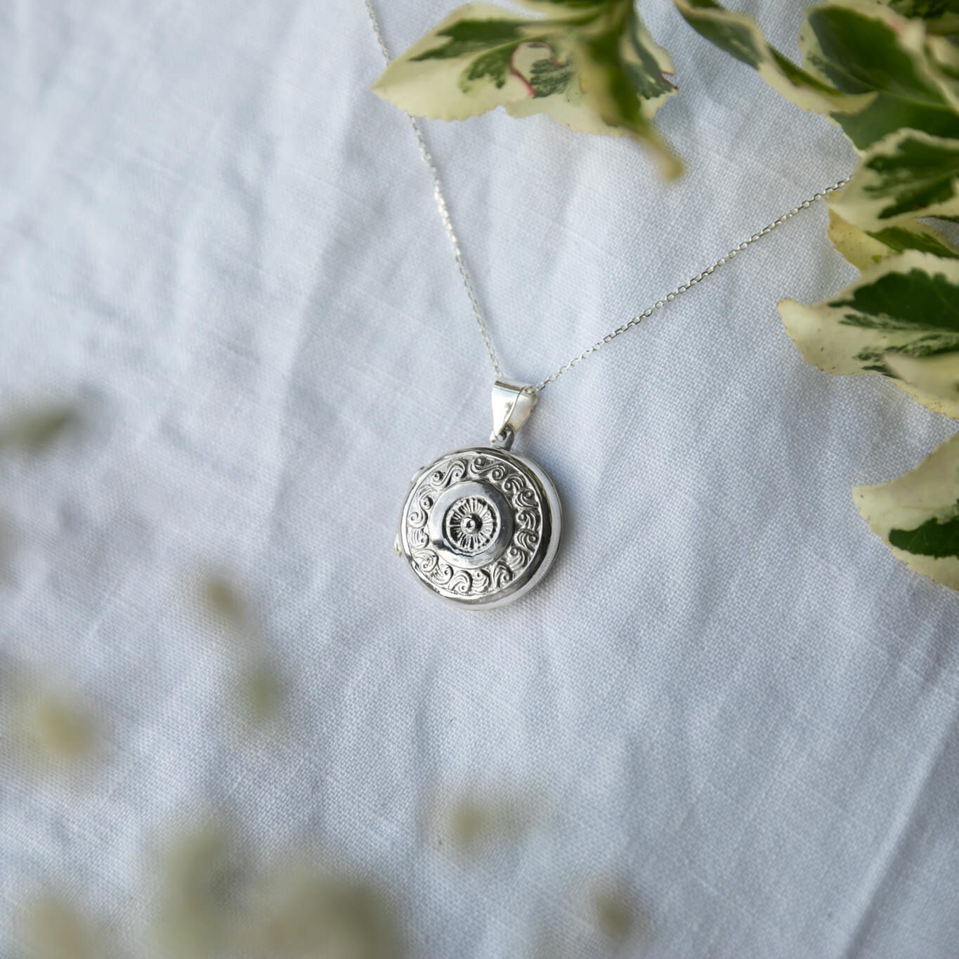 Large round silver locket on a white linen background
