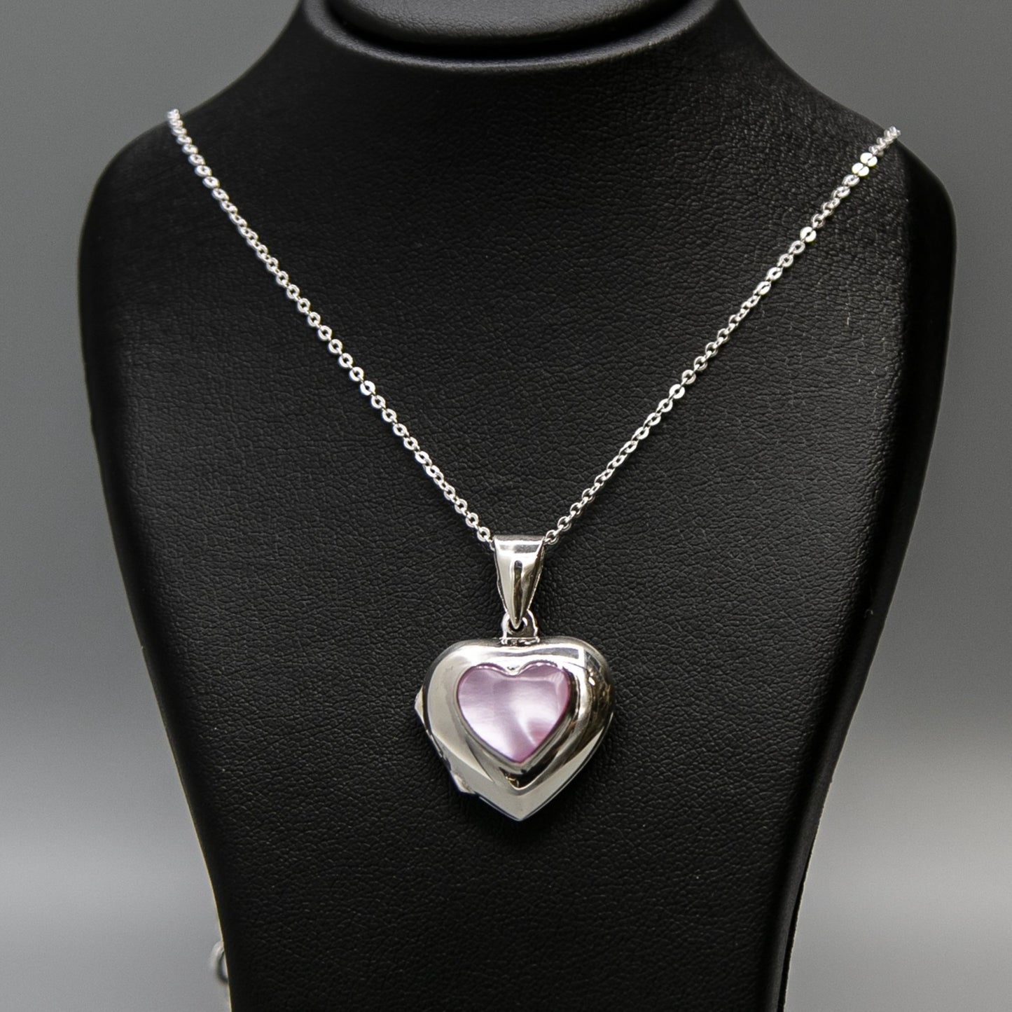 Silver heart-shaped photo locket necklace with pink mother of pearl inset with a silver Italian chain displayed on a black bust.
