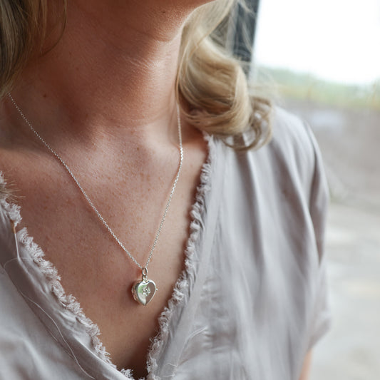 Model wearing heart shaped locket with diamond. Wearing a grey top.