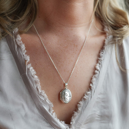Model wearing grey top wearing silver oval locket necklace