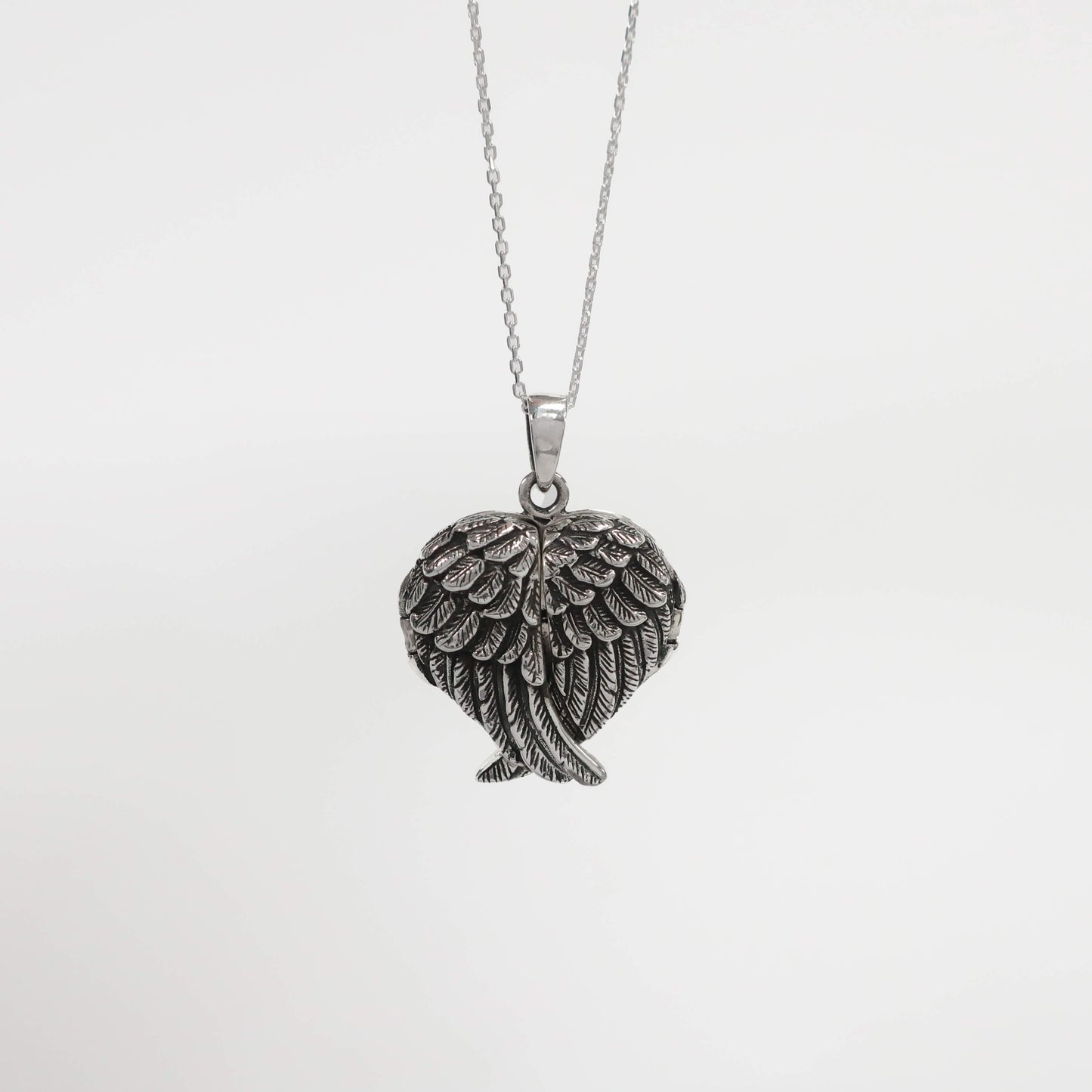 Silver angel wing pendant on a chain against a light gray background
