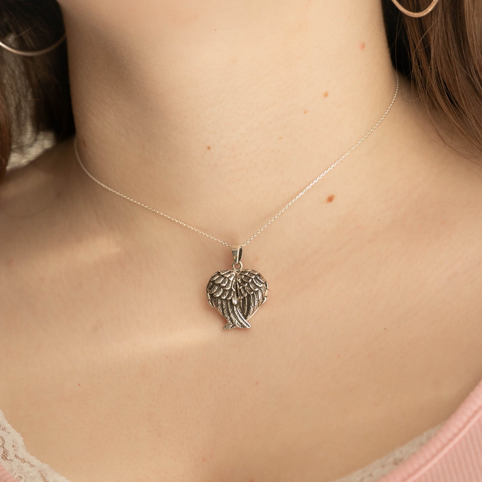 Silver necklace with a winged heart pendant on a person's neck