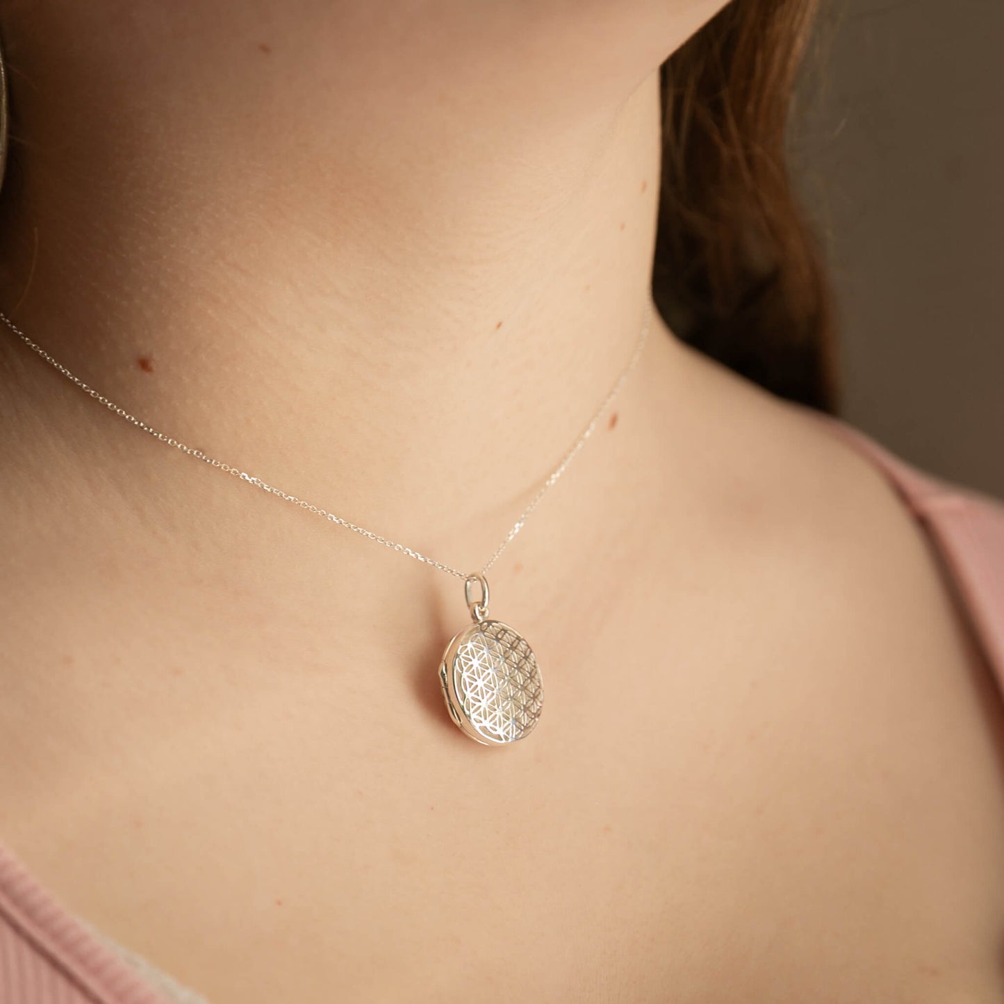 Silver locket necklace with a textured pendant on a person wearing a pink top.
