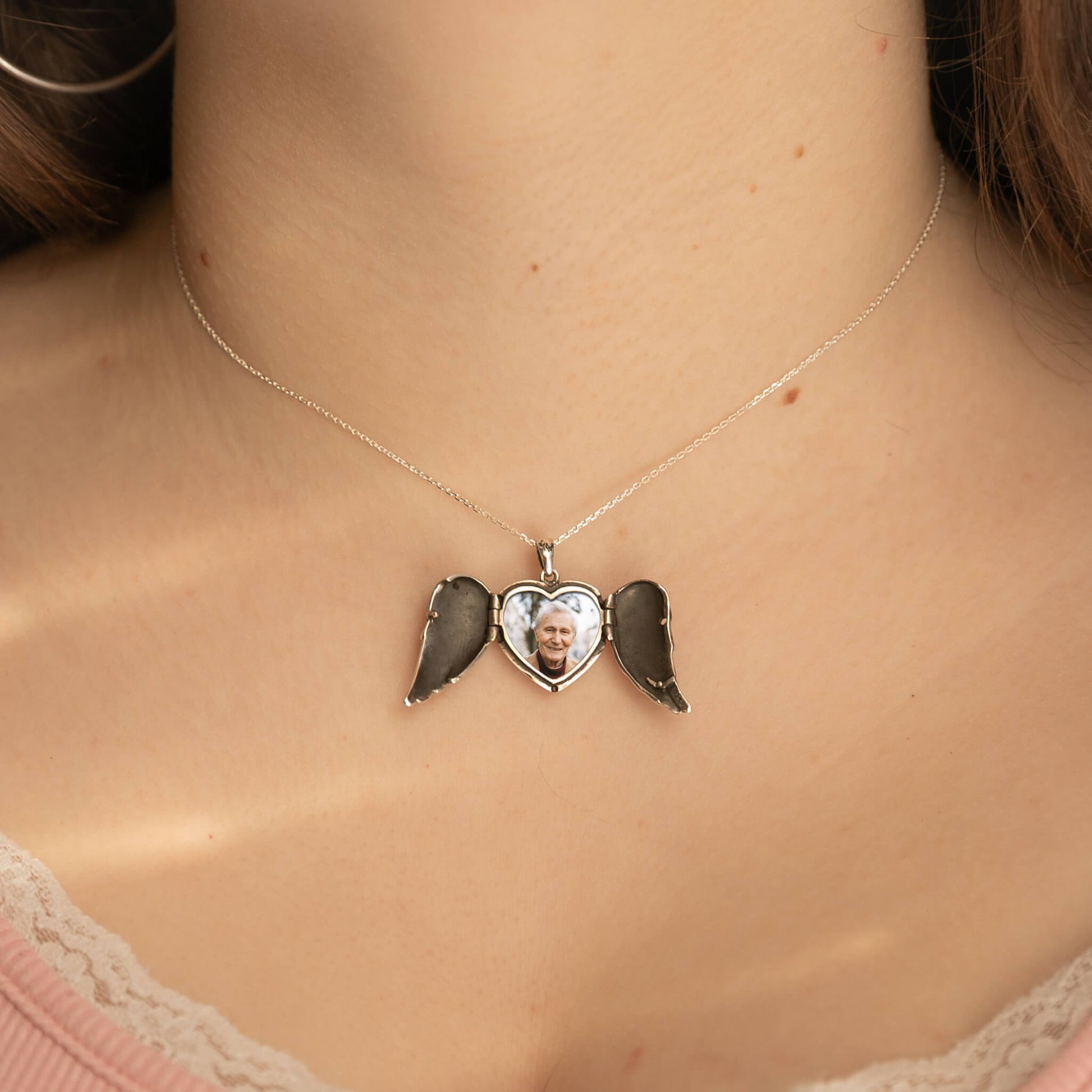 Necklace with a heart-shaped pendant with wings on a person's neck.