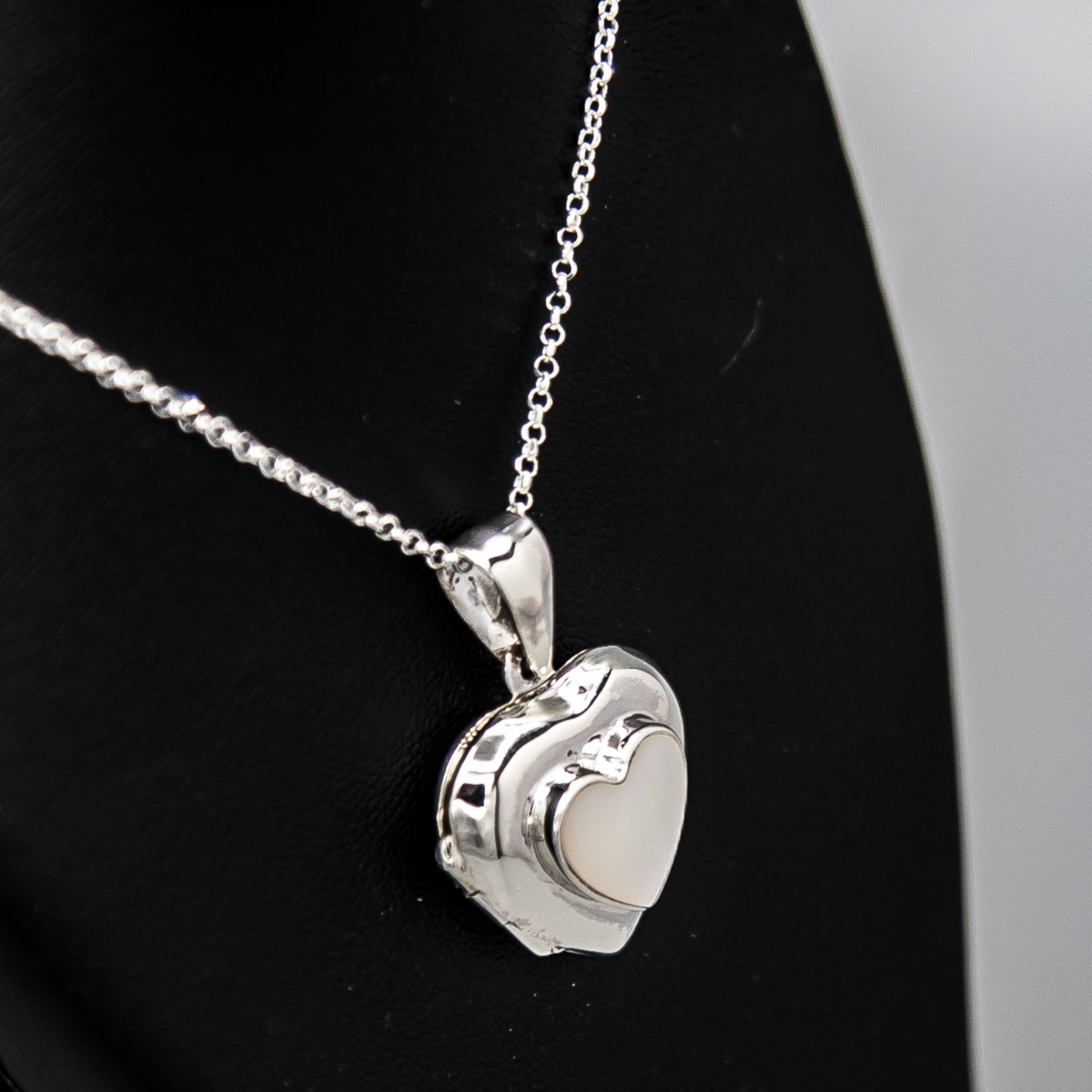 Silver heart shaped photo locket pendant with white mother of pearl inset with a silver Italian chain displayed on a black bust.