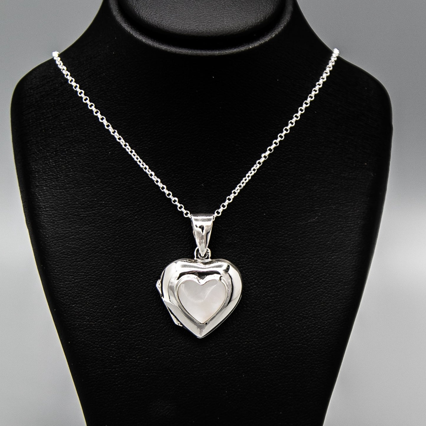 Silver heart shaped photo locket pendant with white mother of pearl inset with a silver Italian chain displayed on a black bust.