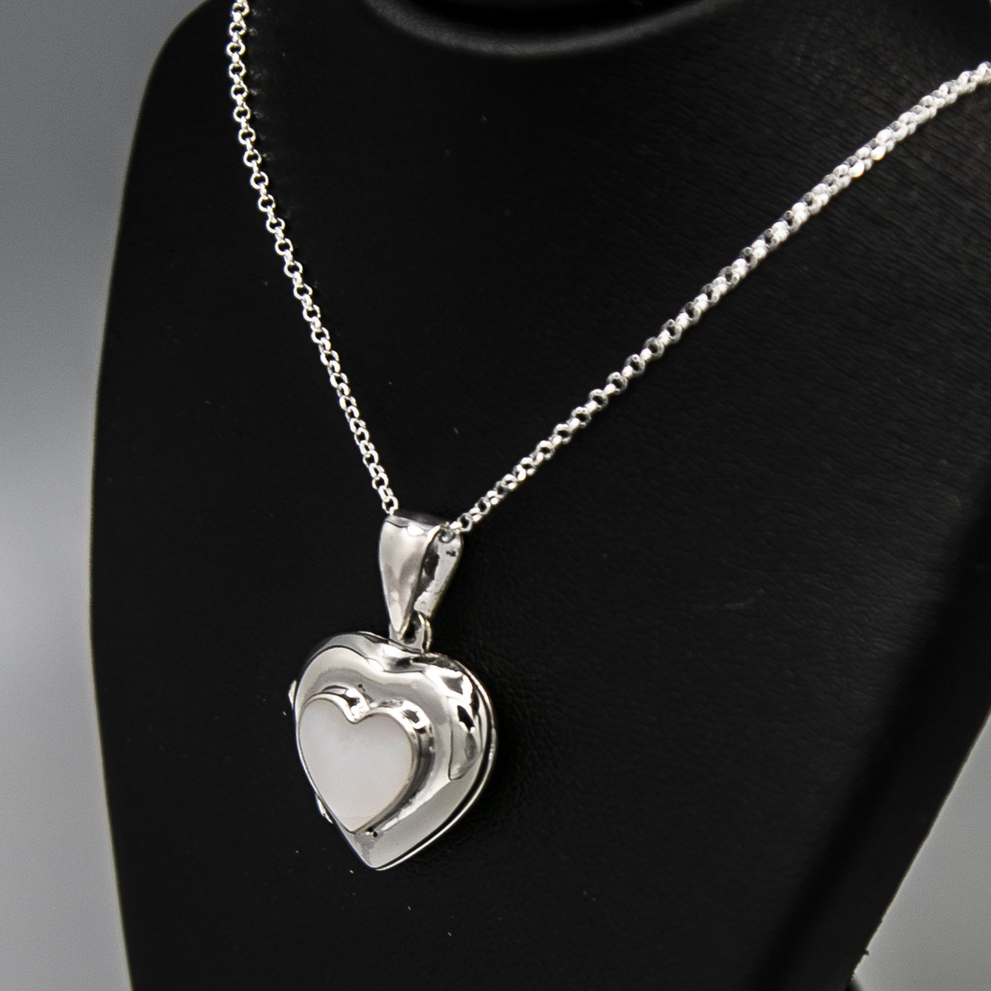 Silver heart shaped luxury locket pendant with white mother of pearl inlay with a silver Italian chain displayed on a black bust.